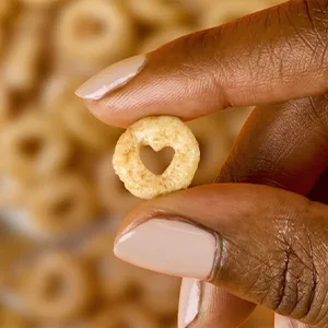 Multi Grain Cheerios Breakfast Cereal - Multi Grain - 18 Oz. - Two fingers holding up a heart shaped multi grain Cheerio.