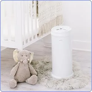 Ubbi Steel Diaper Pail Odor Locking No Special Bag Required Award-Winning Registry Must-Have Slate - Der Ubbi Windeleimer befindet sich in einem reinen, weißen Kinderzimmer, rechts und in der Nähe einer Krippe und Elefantenplüsch.