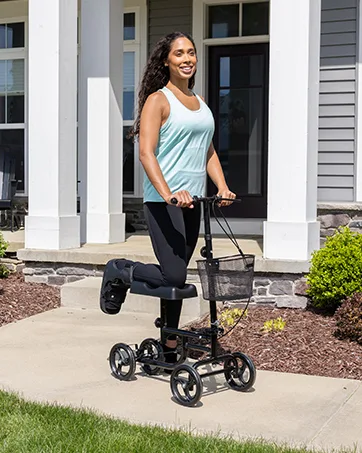 BodyMed Sure-Fit Two-Pull Lumbosacral Support Black Regular Lower Back Stabilizer Secure Lumbar Wrap to Support & Stabilize Core Muscles All-Day Support at Home in The Office & Gym - Woman using the BodyMed Knee Walker on the sidewalk in front of a home.