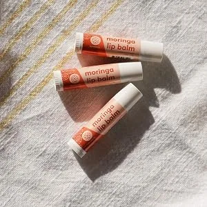 True Moringa Lip Balm - Intense Hydration & Relief for Dry Chapped Lips with Moringa and Shea Butter - 100% vegan paraben free sulfate free ethically sourced - 3 moringa lip balm tubes laying on a bath towel
