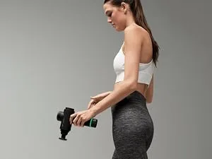 Hyperice Hypervolt Go 2 in Black - Featuring Quiet Glide Technology - Handheld Percussion Massage Gun | 3 Speeds 2 Interchangeable Heads | Helps Relieve Sore Muscles and Stiffness | FSA-HSA Eligible Hypervolt Go 2 Black - Man in a modern gym setting using a Hypervolt 2 Pro on his shoulder.