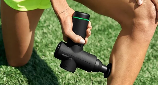Hyperice Hypervolt Go 2 in Black - Featuring Quiet Glide Technology - Handheld Percussion Massage Gun | 3 Speeds 2 Interchangeable Heads | Helps Relieve Sore Muscles and Stiffness | FSA-HSA Eligible Hypervolt Go 2 Black - Woman sitting on a couch holding a Hypervolt Go 2