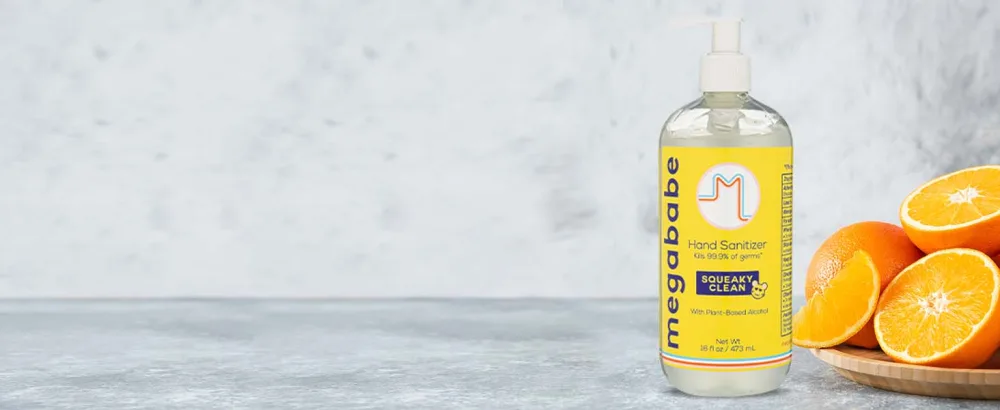 Megababe Squeaky Clean Hand Sanitizer Pump 16oz - Hand Sanitizer on grey background next to oranges.
