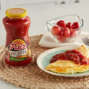 Pace Nacho Jalapeno Queso Dip, Great for Nachos, 15 Ounce Jar - Table setting including jar of Pace picante, bowl of fresh cherries, and salsa covered omelet