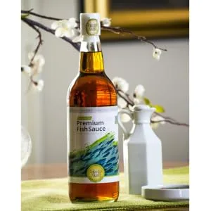 Four Elephants Premium Fish Sauce 25 Ounce Certified Non-GMO and Gluten Free (1 Pack) - Fish sauce on table with cherry blossoms in background.