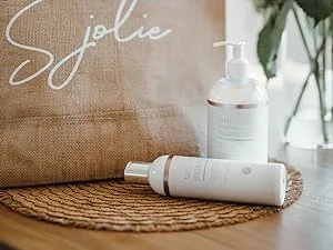 SJOLIE Spray Tan Solution - Luxe 12 - Violet Based Dark Blend | Sunless Tanning Solution for Deep Dark Bronze Finish All Natural (8oz) 8 Fl Oz (Pack of 1) - bottle of moisturizer and tan extend lotion on a table next to a tote bag and flowers