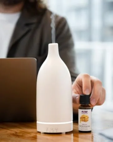 Now Foods Camphor Oil (Cinnamomum camphora)30mL - NOW essential oils and diffuser on desk near man working on laptop