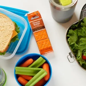 Austin Sandwich Crackers, Single Serve Snack Crackers, Office and Kids Snacks, Peanut Butter on Cheese, 11oz Tray (8 Packs) - Peanut butter crackers in a lunchtime scene with a sandwich nuts juice and crudite on a table
