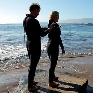 Aloe Cadabra Ocean Safe Lube - Standing Man on the left assisting standing woman on the right to zip up her wetsuit to go swimming