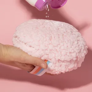Megababe Body Powder Applicator - Dust Puff | Oversize (6 x 3) Powder Puff | Powder Sold Separately - Pink background. Hand holding Dust Puff, bottle of Body Dust is open, pouring powder on puff.