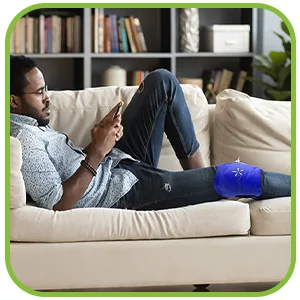 TheraPAQ Ice Packs for Injuries Reusable Version - Adjustable 14 x 6 Inch Hot and Cold Gel Pack w/Adjustable Strap for Shoulder, Knee, Back, Ankle, and Foot Discomfort - Sports Therapy and Recovery Gel Pack & Flexible Strap - Man relaxing on the couch with the hot/cold pack on his knee