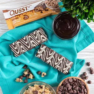 Quest Nutrition Dipped Chocolate Chip Cookie Dough Protein Bars, High Protein, Low Carb, Gluten Free, Keto Friendly, 12 Count - image of 2 dipped cookie dough bars on a table with chocolate chips
