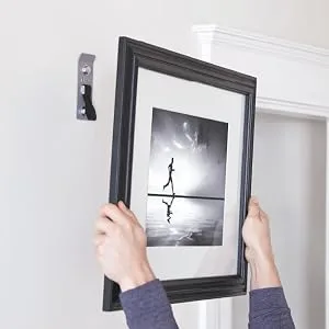 TRX Training Invizi-Mount Wall Anchor V2 Suspension Training Kit, Training Club App INVIZI-MOUNT 2 - A person using an exercise wall mount to hang a picture frame.