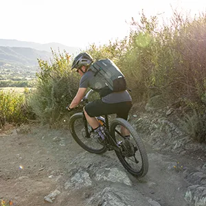 CamelBak M.U.L.E. Pro 14 Bike Hydration Backpack 100oz - Body Mapping Technology Agave Green/Black - Man wearing a MULE Pro hydration backpack while riding on a mountain trail.