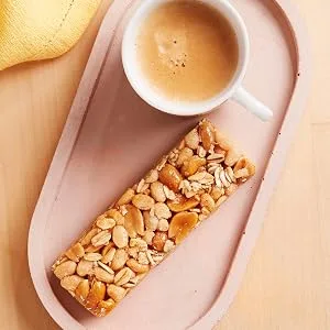 Nature Valley Sweet & Salty Nut Roasted Peanuts Cereal Bars 4 x 30g Pack of 8 total 32 Bars - Sequentiële afbeeldingen van noten of snacks die worden geserveerd in gebogen, beige keramische schalen tegen een warme achtergrond.