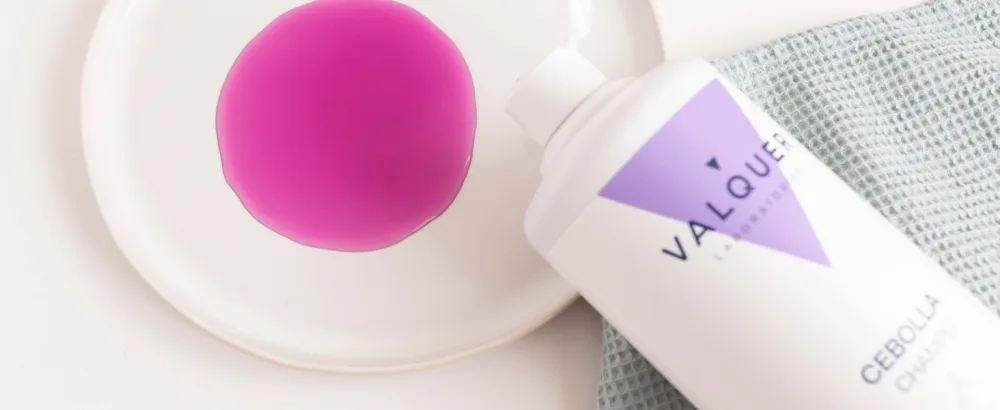 Valquer Laboratorios Cuidados Onion shampoo Reduce fat Hair Stimulant 1L Pack of 12 units - Roze spons voor het mengen van cosmetica op een wit oppervlak naast een verpakking met een paars label voor schoonheidsproducten