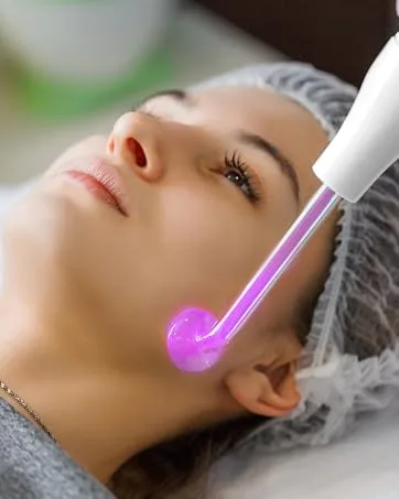 iklestar Dermapen A8S Professional Microneedling Pen with 18 Pcs 12Pin 36Pin Replacement Needle Cartridges Wireless or Wired Mode 2 Mudules Derma Pen 6 Speed Levels and 025 mm Depth Adjustable - Close-up van de gezichtsbehandeling met een draagbaar apparaat met een gloeiende paarse punt op de wang van de klant. De cliënt draagt tijdens de procedure een beschermende haarkap.