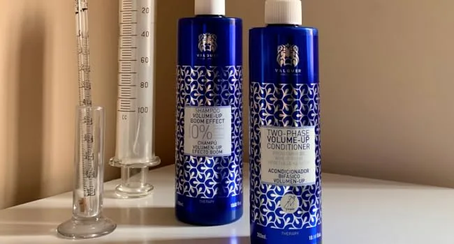 Valquer Laboratorios V lquer Shampoo VolumeUp Boom Effect 400 ml - Twee kobaltblauwe flessen met sierlijke geometrische patronen en witte etiketten. Laboratoriumglaswerk inclusief maatcilinders op de achtergrond