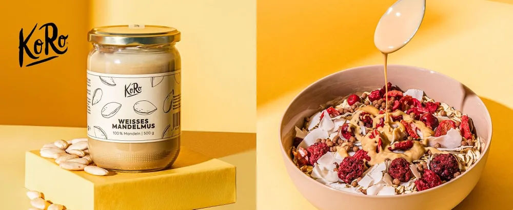  KoRo KoRo - Chilli flakes 500 g - Un bocal en verre de beurre de cajou KoRo à côté d'un bol de yogourt garni de baies, de noix et de miel arrosé. L'étiquette du pot montre une illustration de noix de cajou