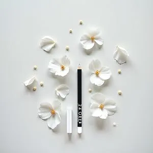  DEBORAH Deborah Matita Labbra 24ORE Universal Transparent suitable for all tones of Robin when applied first to all lips helps extend its hold - Pétales de fleurs blanches éparpillés et petits objets disposés artistiquement sur fond gris clair dans un style minimaliste.