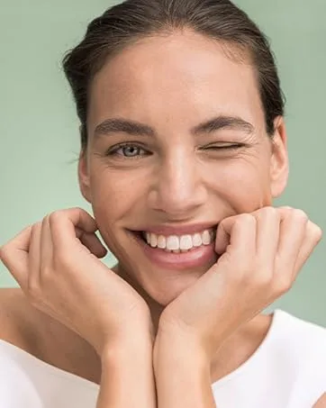  lavera lavera Hydro Refresh Cream Gel - With algae and hyaluronic acid - Noticeable cooling effect - Vegan - Natural cosmetic - 50 ml - Gros plan d'une personne souriante avec des dents blanches brillantes qui clignent d'un œil. Ses mains sont positionnées dans une pose joyeuse sur un fond vert clair près de leur visage