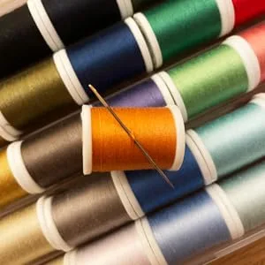 LEONIS 30 Color Handy Polyester Sewing Threads 45 m / 50 yds Each   93011   A.50yd - orange thread spool with needle pierced through, on top of thread spools in other colors