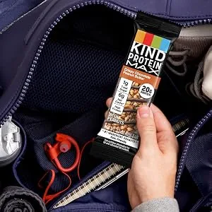 KIND Protein MAX Raspberry Cocoa Crisp 20g Protein 1g Sugar Low Sugar High Protein Snack Bars 4 Count 1 Count (Pack of 4) - A person grabbing a KIND PROTEIN MAX Crispy Chocolate Peanut Butter Bar out of their bag
