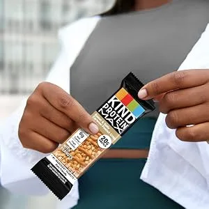 KIND Protein MAX Raspberry Cocoa Crisp 20g Protein 1g Sugar Low Sugar High Protein Snack Bars 4 Count 1 Count (Pack of 4) - A person holding a KIND PROTEIN MAX Sweet and Salty Caramel Peanut Crisp bar