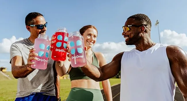 DripDrop Hydration Packets - Bold Variety Pack - Single Serve Electrolytes Powder Drink Mix - Watermelon Berry Lemon Orange - Non-GMO Gluten Free Vegan - 80 Sticks - Three people in workout gear clinking DripDrop water bottles together smiling