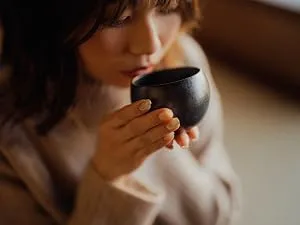 Your ExcellenTEA Earl Grey Blue Loose Leaf Black Tea Bergamot Ceylon Black Tea with Cornflower Petals Floral Earl Grey Blend - 250g  - A person holding a small, round, black ceramic cup or bowl close to their face, as if about to drink from it.