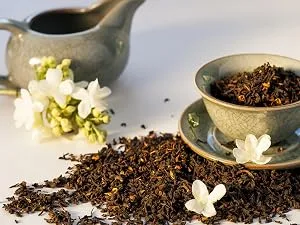 Your ExcellenTEA Earl Grey Blue Loose Leaf Black Tea Bergamot Ceylon Black Tea with Cornflower Petals Floral Earl Grey Blend - 250g  - Loose tea leaves scattered on a surface, with a ceramic teacup and saucer filled with tea leaves. A gray teapot and white flowers are visible in the background.