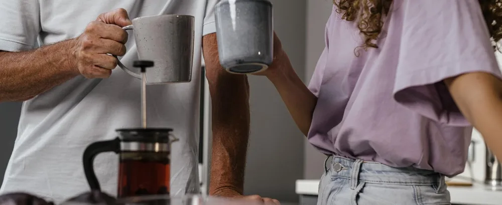 Your ExcellenTEA Earl Grey Blue Loose Leaf Black Tea Bergamot Ceylon Black Tea with Cornflower Petals Floral Earl Grey Blend - 250g  - Two people holding large gray ceramic mugs in a kitchen setting. A French press coffee maker is visible on the counter in the foreground.