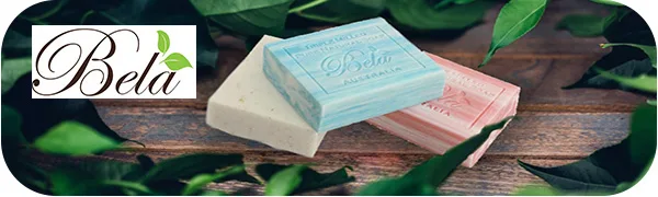 Bela Assorted Triple French Milled Moisturizing Soap Bars No Harsh Ingredients 3.3 oz each - 6 Pack - Three Bela soap bars on wooden planks with leafy greenery and Bela logo.