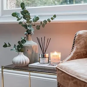 Neom Organics London Scented Candle 420g De-Stress Candle - Neom reed diffuser and wellbeing candle on a side table next to an armchair